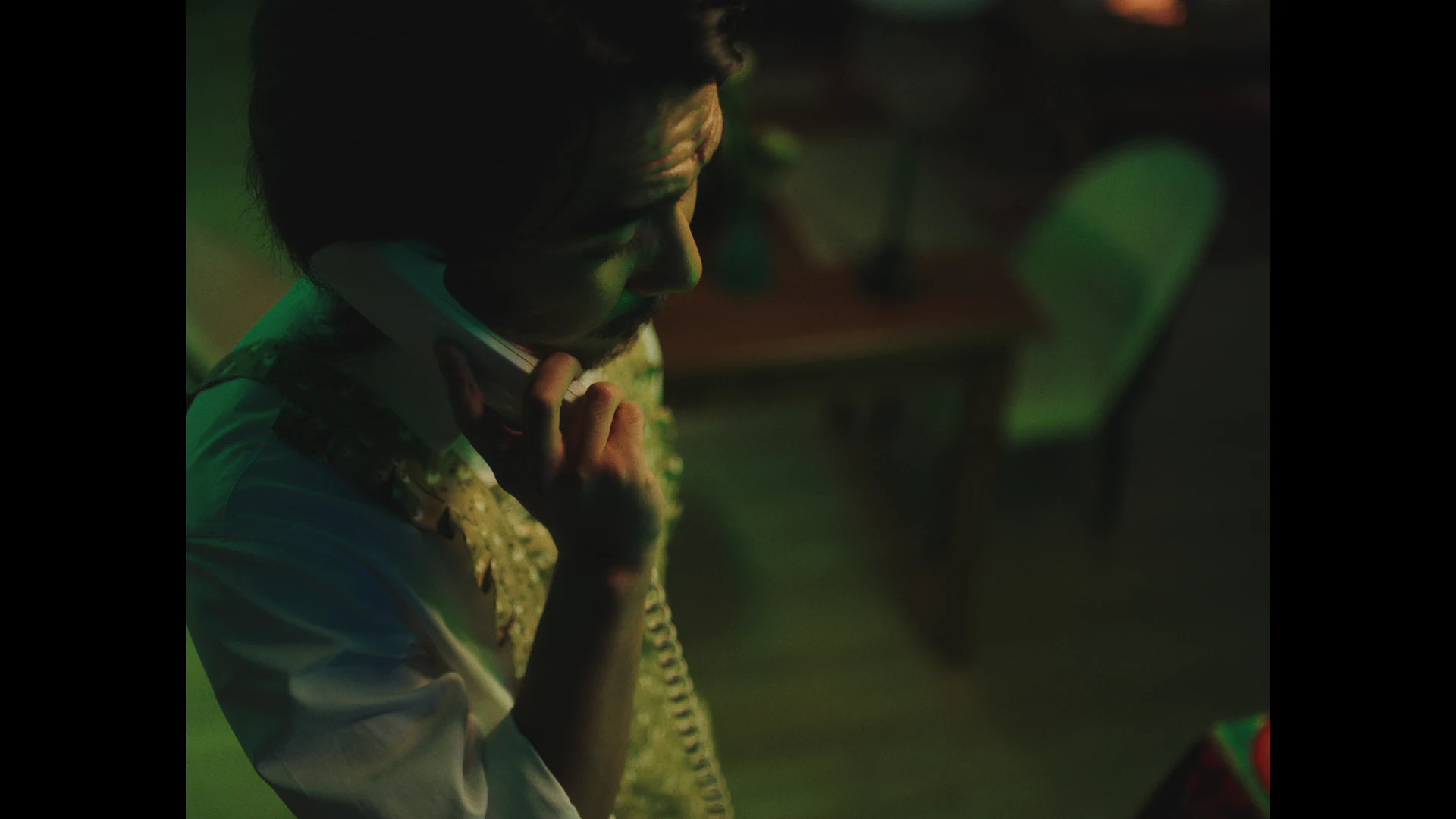 A man holds a telephone against his cheek in the green-lit dining room