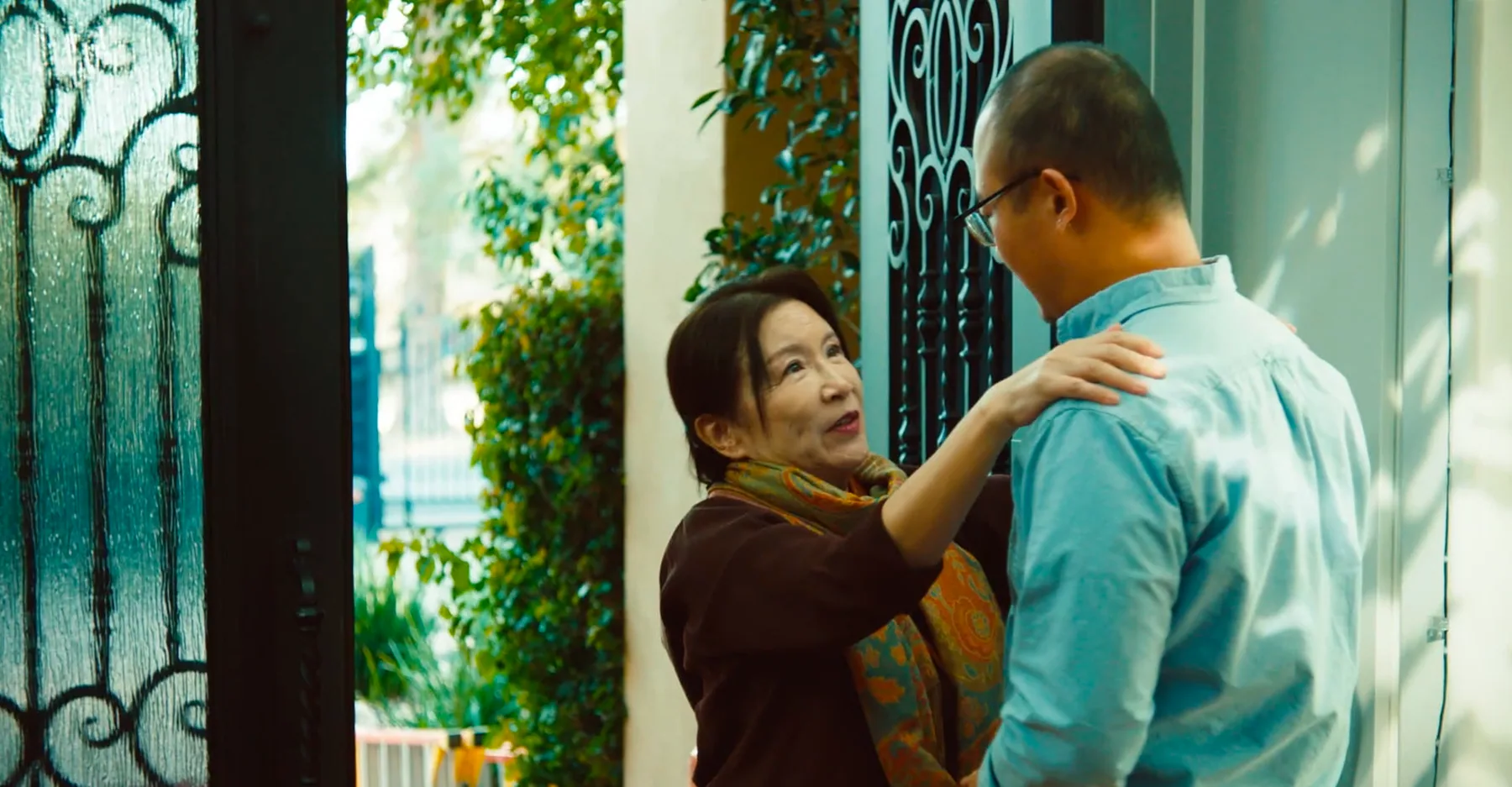 A mother greets her son in a bright doorway