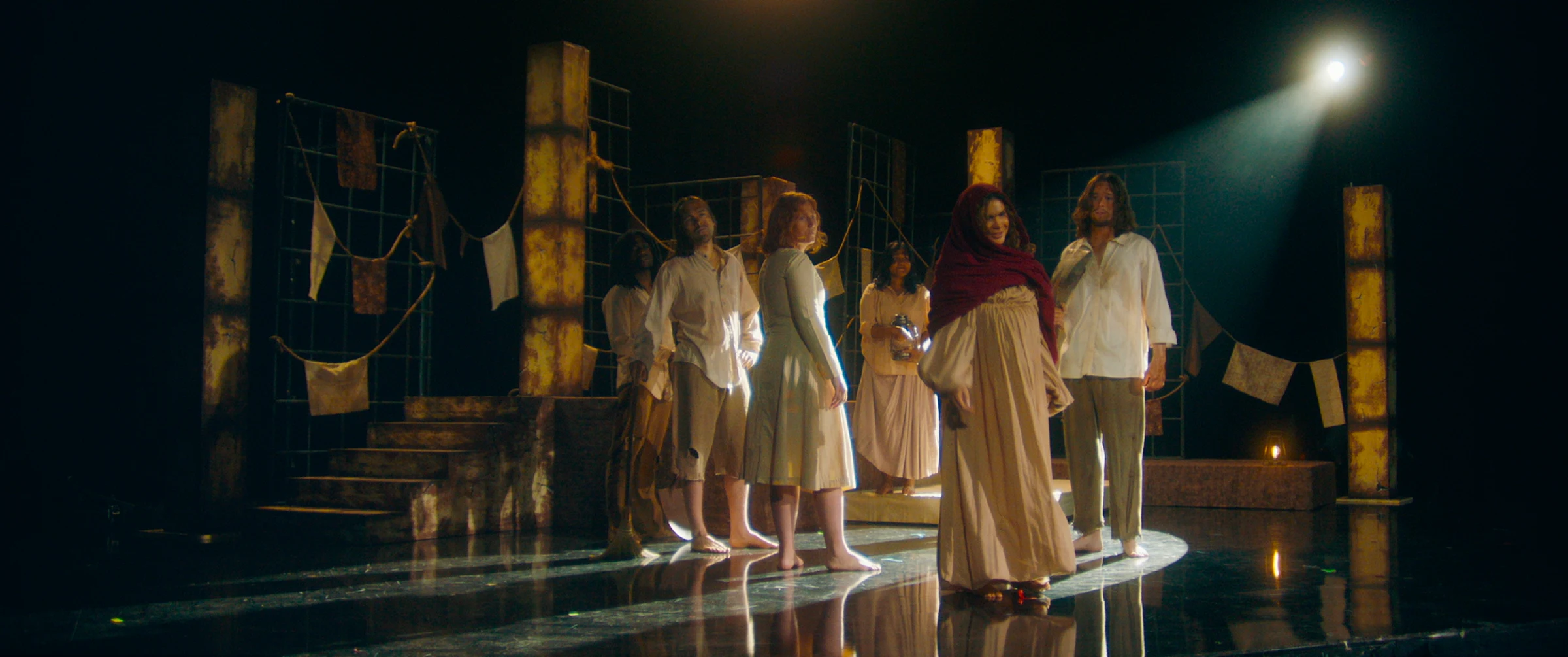 The Witch Lament ensemble arranged across a reflective theatrical stage