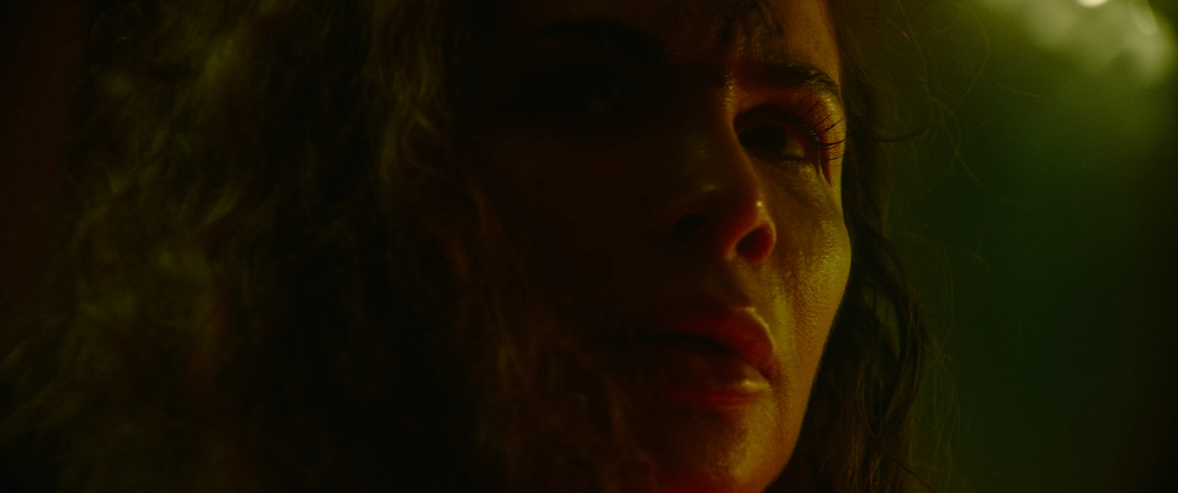 An intimate green and amber close-up of the central woman in Witch Lament